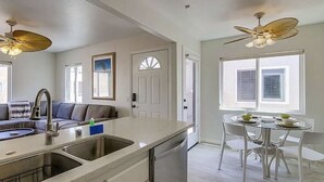 A modern kitchen with a central island, a dining area with a round table, and a ceiling fan.