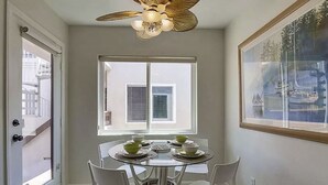A dining area with a round table, white chairs, and a ceiling fan.