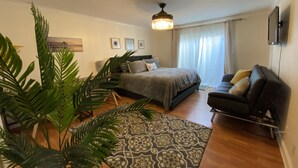 Een moderne slaapkamer met een bed, een sofa, een grote plant en een kamerbreed tapijt met een patroon.