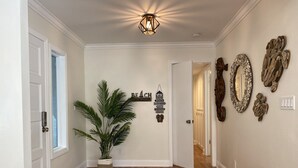 Een gang met houten vloer, een potplant, decoratieve wandkunst en een plafondlamp.