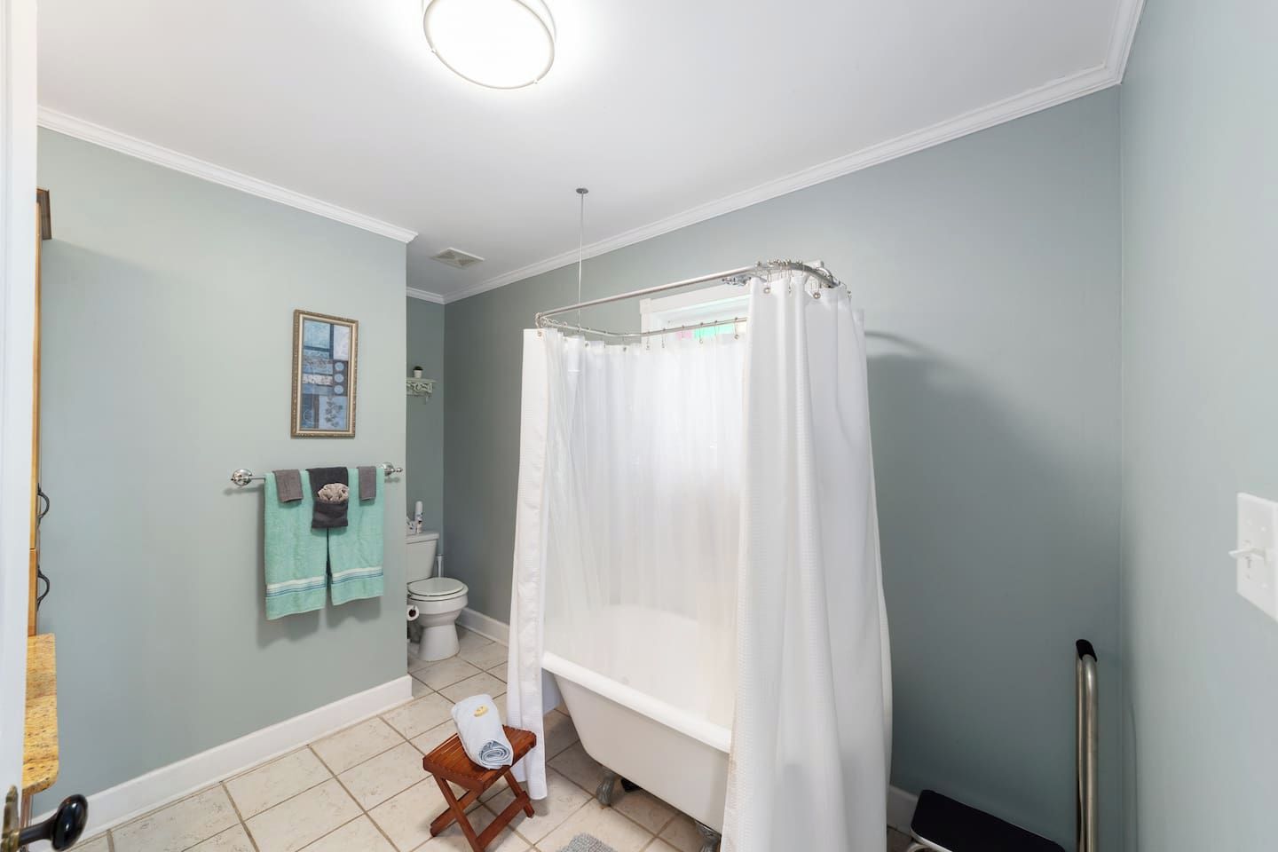 Ein Badezimmer mit Badewanne, Duschvorhang, Toilette und einem kleinen Holzschemel.