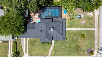 A residential property with a large, dark-colored roof, a swimming pool, and a well-maintained lawn.