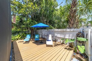 A wooden deck with outdoor furniture, a blue umbrella, and lush greenery. - Private historic district apt with pool-suite B (Ocala)