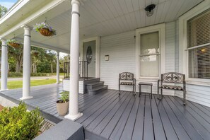 A porch with white columns, a bench, a small table, and hanging flower baskets. - Martin House | Historic Suite with Pool Downtown (Ocala)
