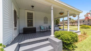 A porch with a bench and chairs, a covered area with columns, and a welcome sign.