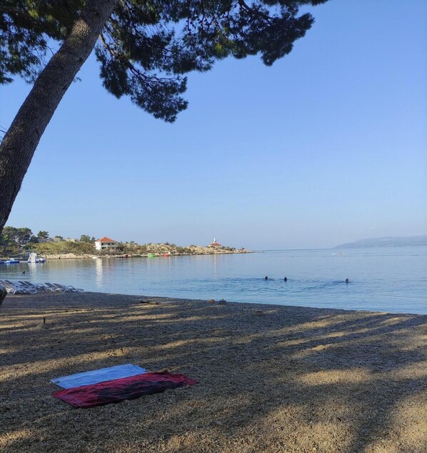 Ein Strand mit blauem Himmel, ruhigem Wasser und ein paar badenden Personen.