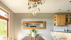 Eine moderne Küche mit einem Holztisch, weißen Stühlen, einer Pendelleuchte und einem großen Spiegel über dem Tisch.
