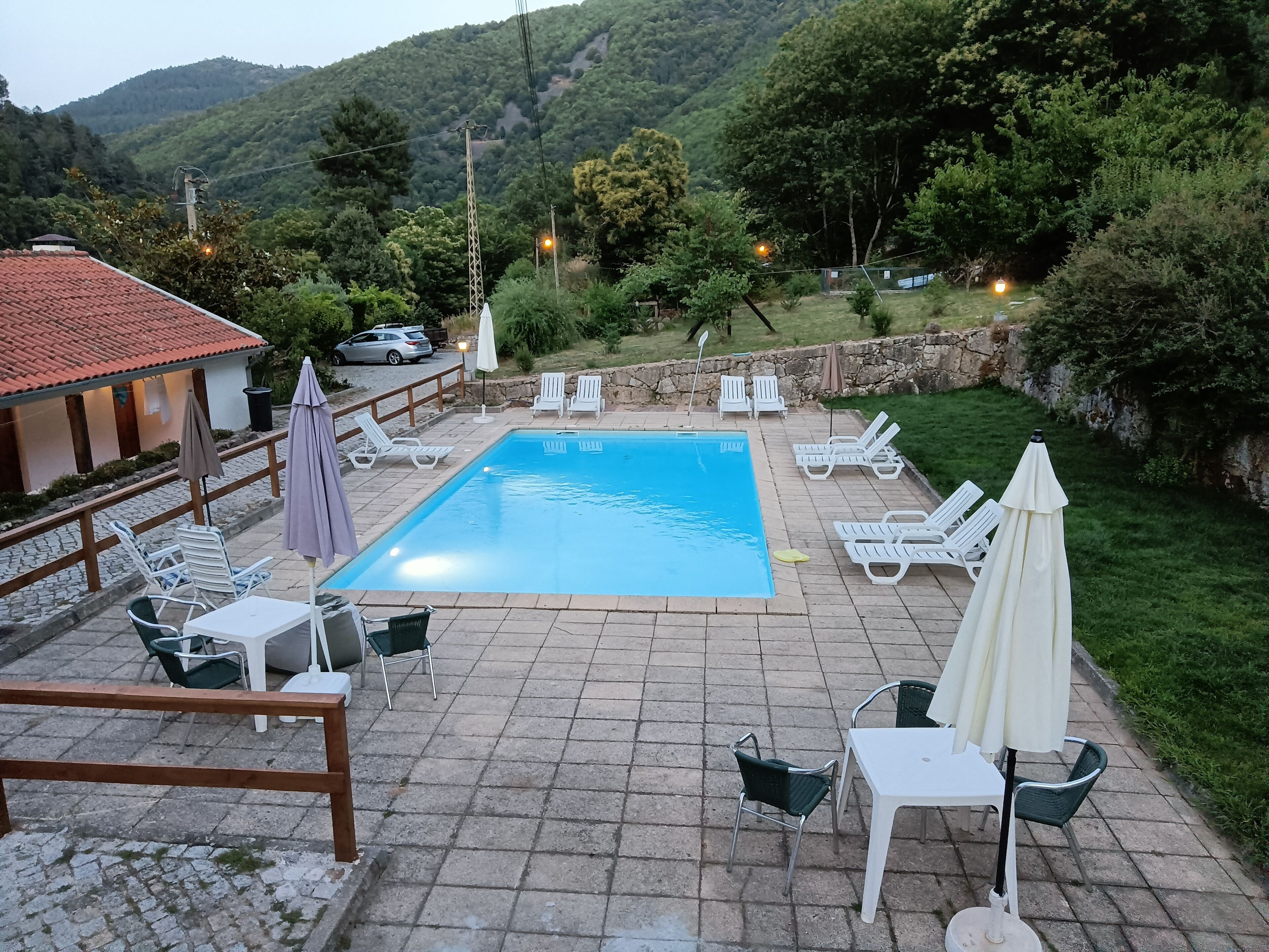 Una piscina con sillones de playa y sombrillas, rodeada por un patio de piedra y un muro de piedra.