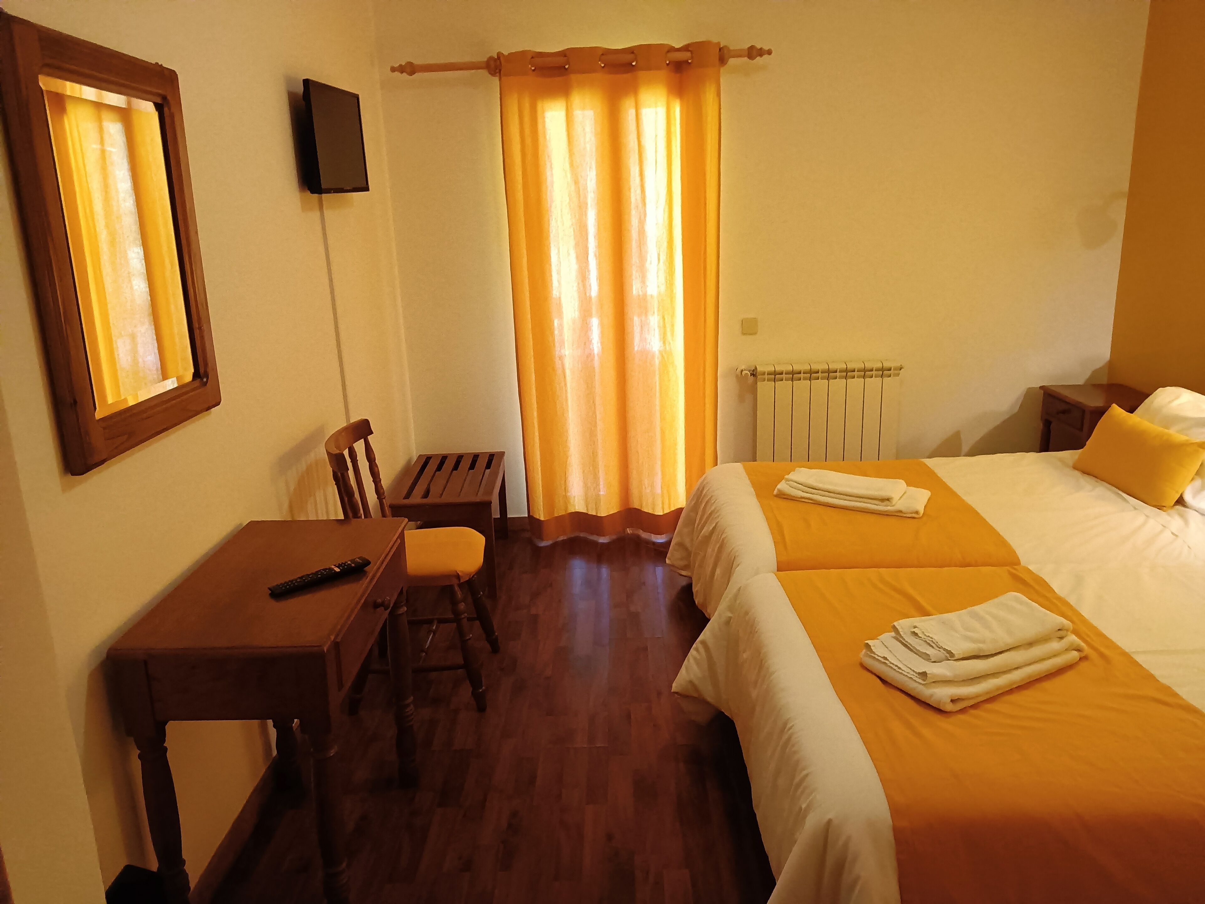 Habitación de hotel con escritorio de madera, una silla, una cama con dos almohadas y un radiador.