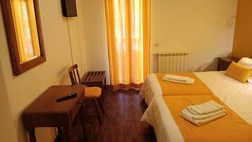 Habitación de hotel con escritorio de madera, una silla, una cama con dos almohadas y un radiador.