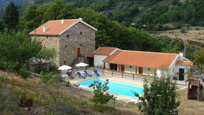 A stone building with a red-tiled roof, a swimming pool, and a garden area with lounge chairs. - Quinta de Leandres (Manteigas)