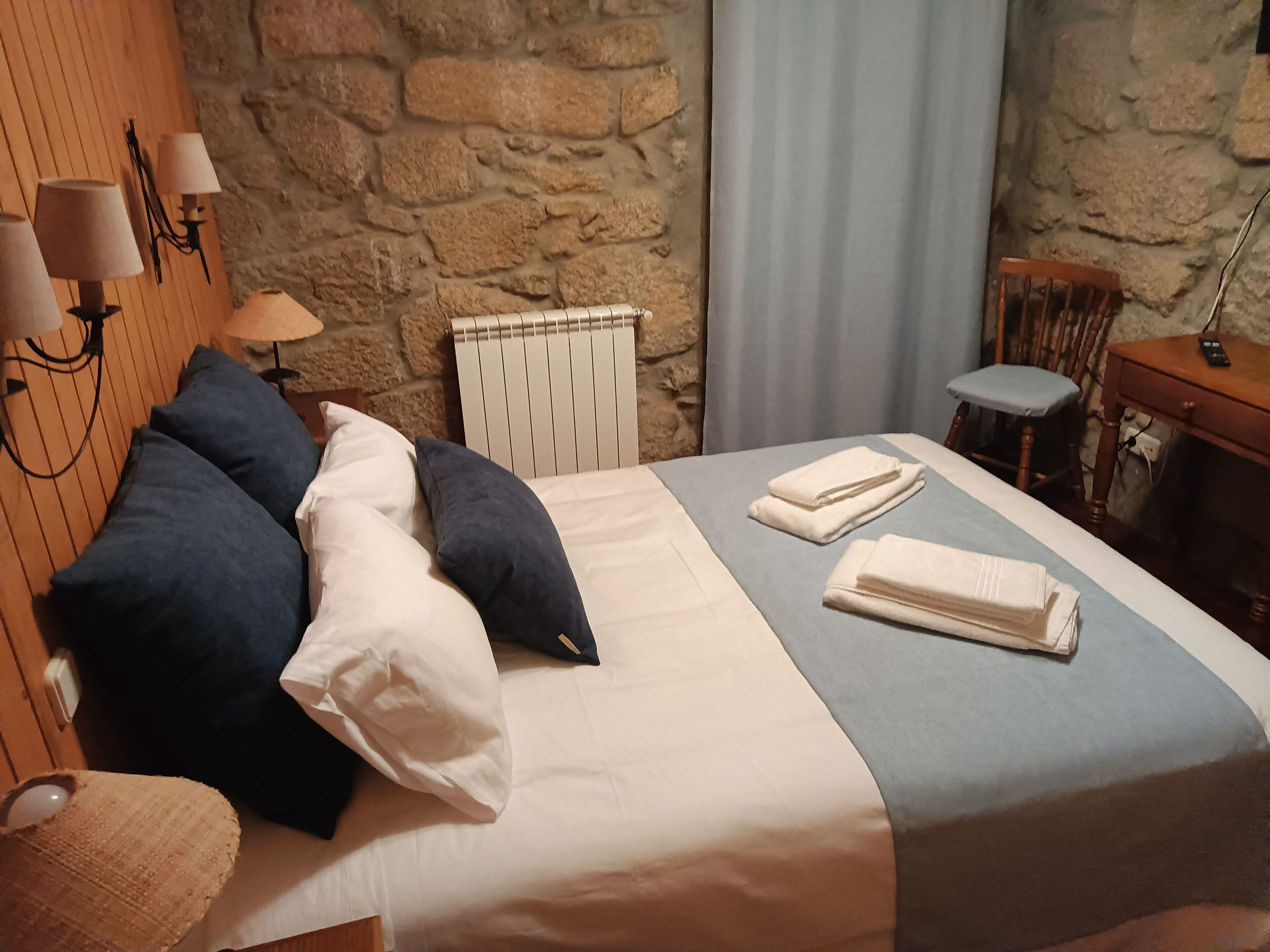 A neatly made bed with pillows, a folded towel, and a bedside table with a lamp.