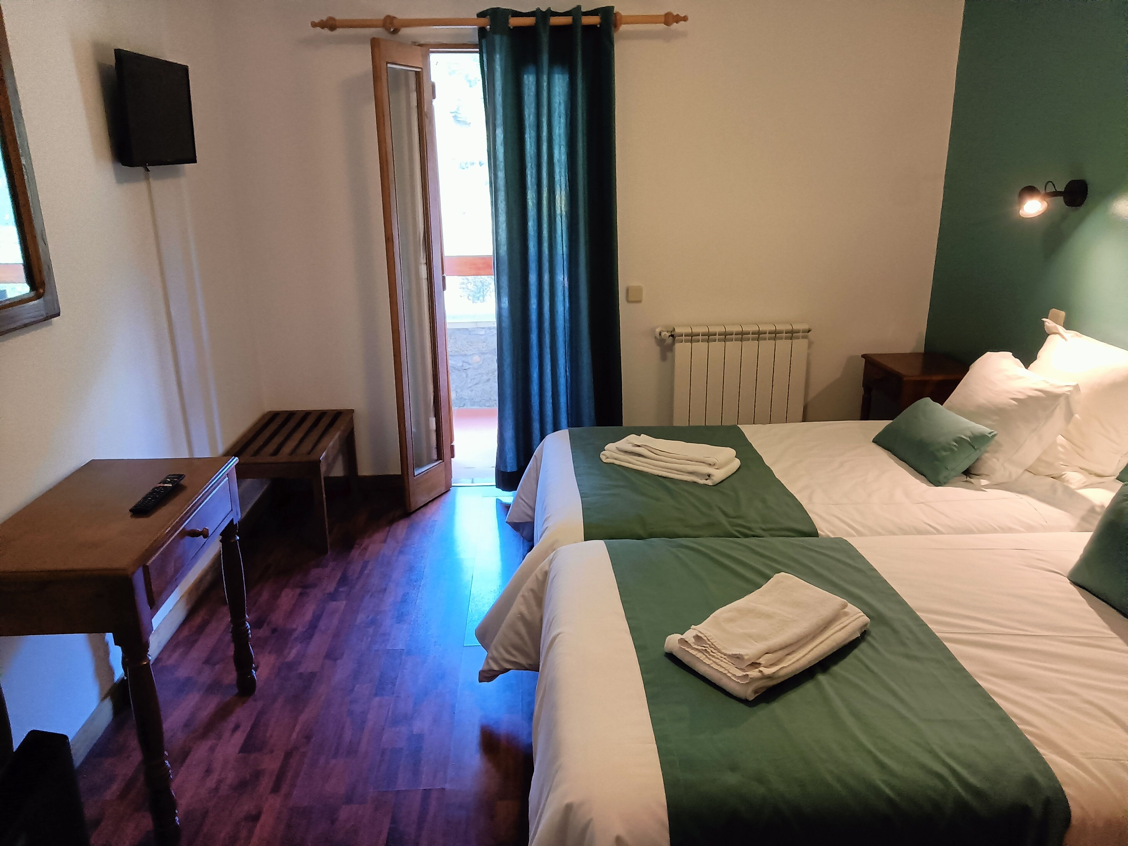 A hotel room with two beds, a desk, a chair, a TV, and a window with curtains.