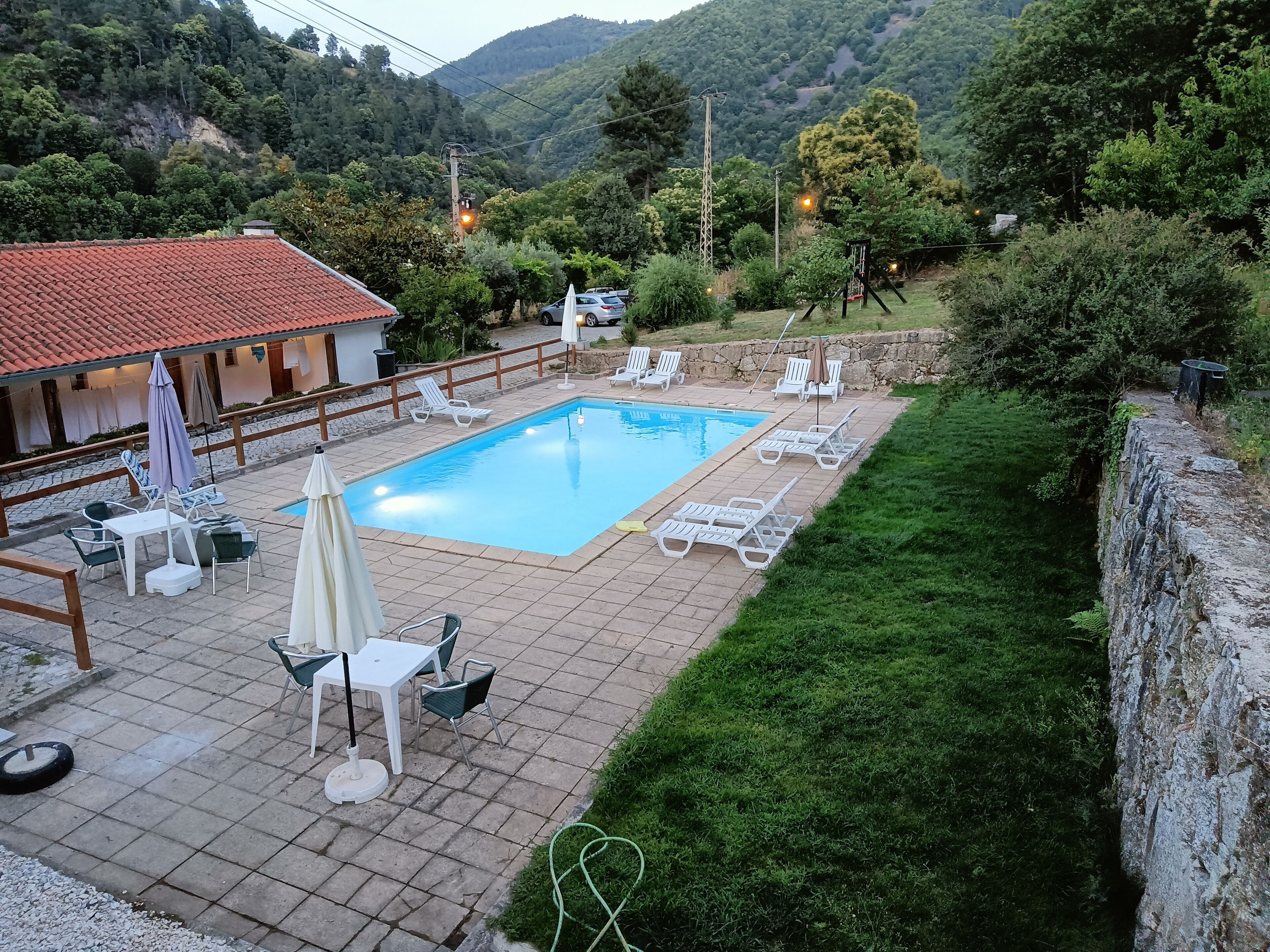 A swimming pool with lounge chairs and umbrellas, surrounded by a stone wall and greenery.