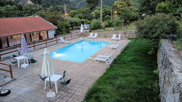 A swimming pool with lounge chairs and umbrellas, surrounded by a stone wall and greenery.