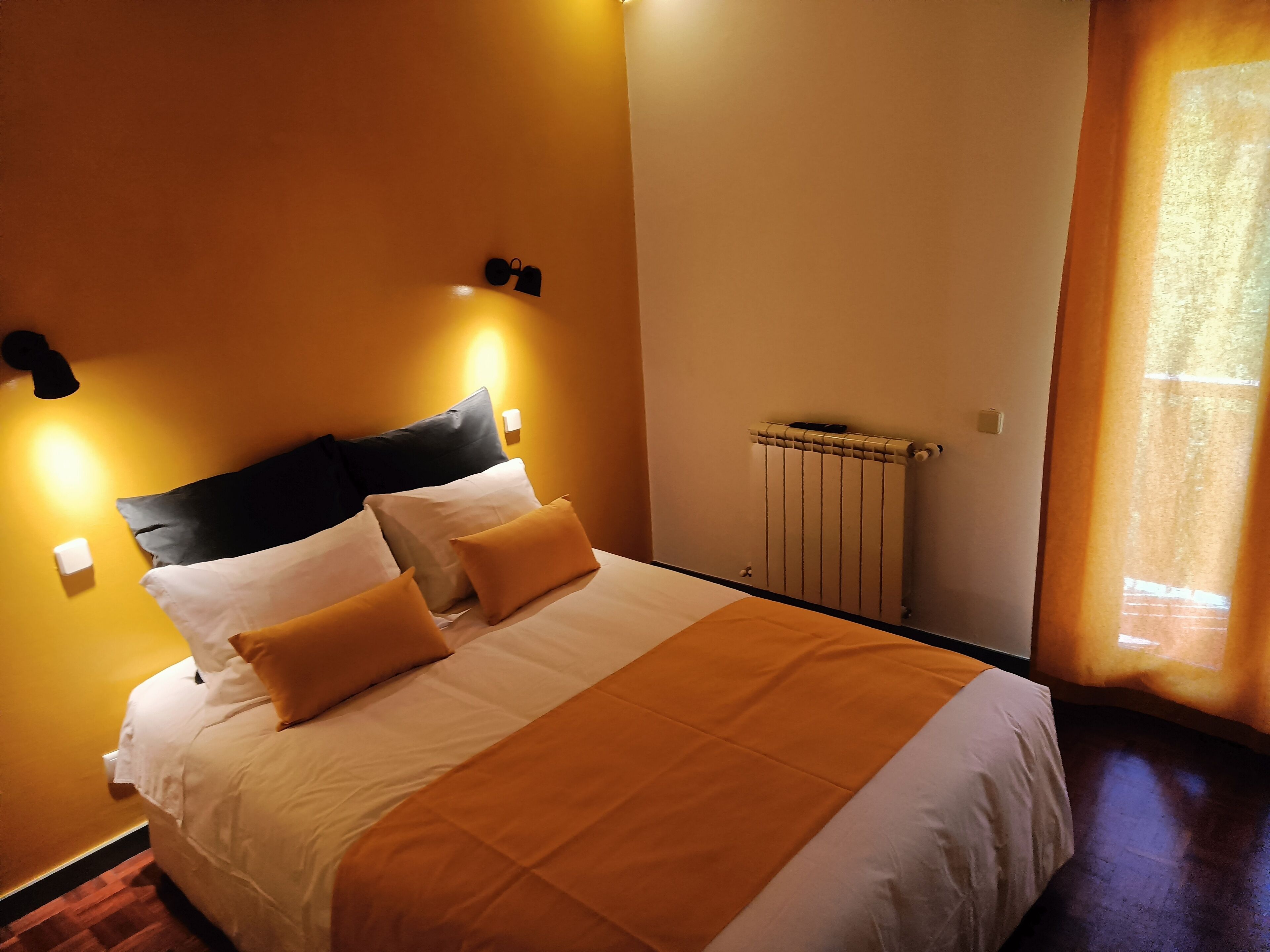 A hotel room with a bed, a radiator, and a window with curtains.