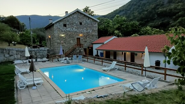 A stone building with a swimming pool, outdoor seating, and a view of mountains. - Quinta de Leandres (Manteigas)