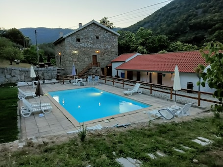 A stone building with a swimming pool, outdoor seating, and a view of mountains.