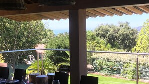 Ein Essbereich im Freien mit Blick aufs Meer, Tische gedeckt mit Weingläsern, und eine Pergola darüber.