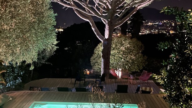 Ein Außenbereich bei Nacht mit Schwimmbad, umgeben von Bäumen und einer Terrasse mit Sitzgelegenheiten.