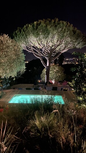 A nighttime outdoor area with a swimming pool, surrounded by trees and a deck with seating.