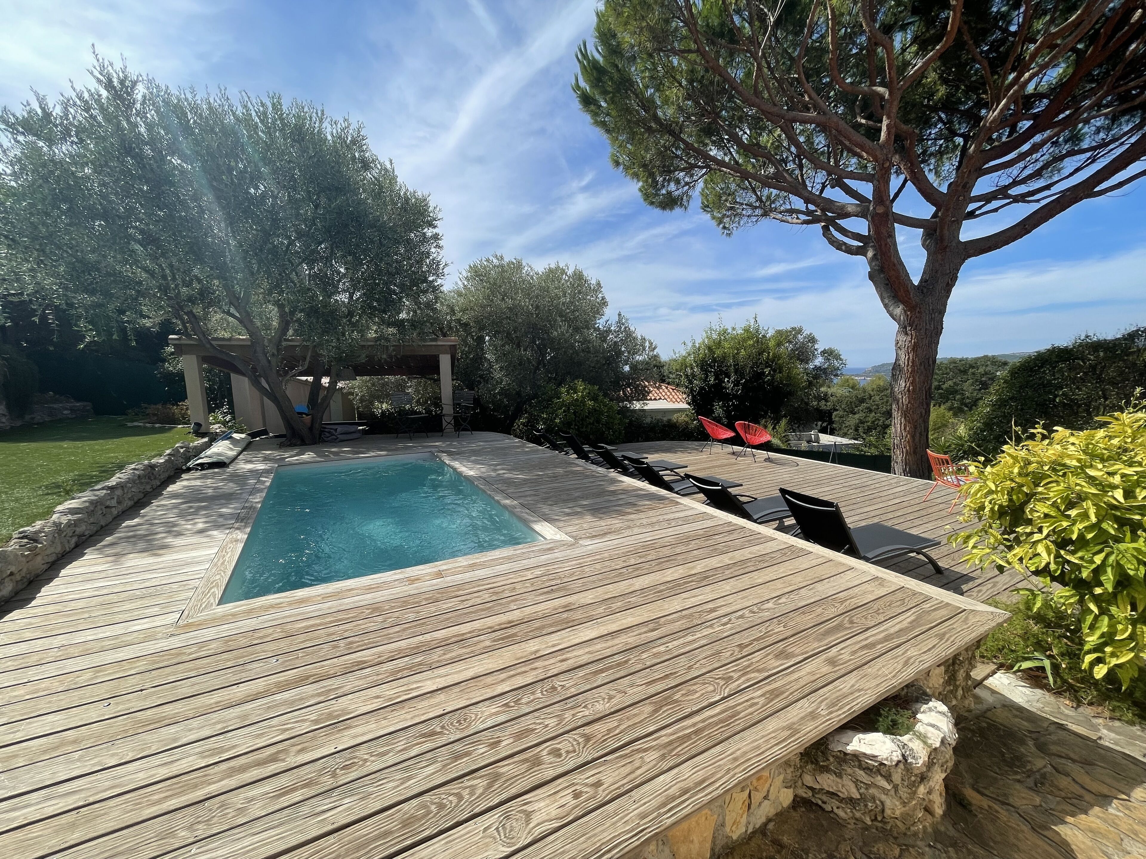 A wooden deck with a pool, outdoor seating, and a pergola.