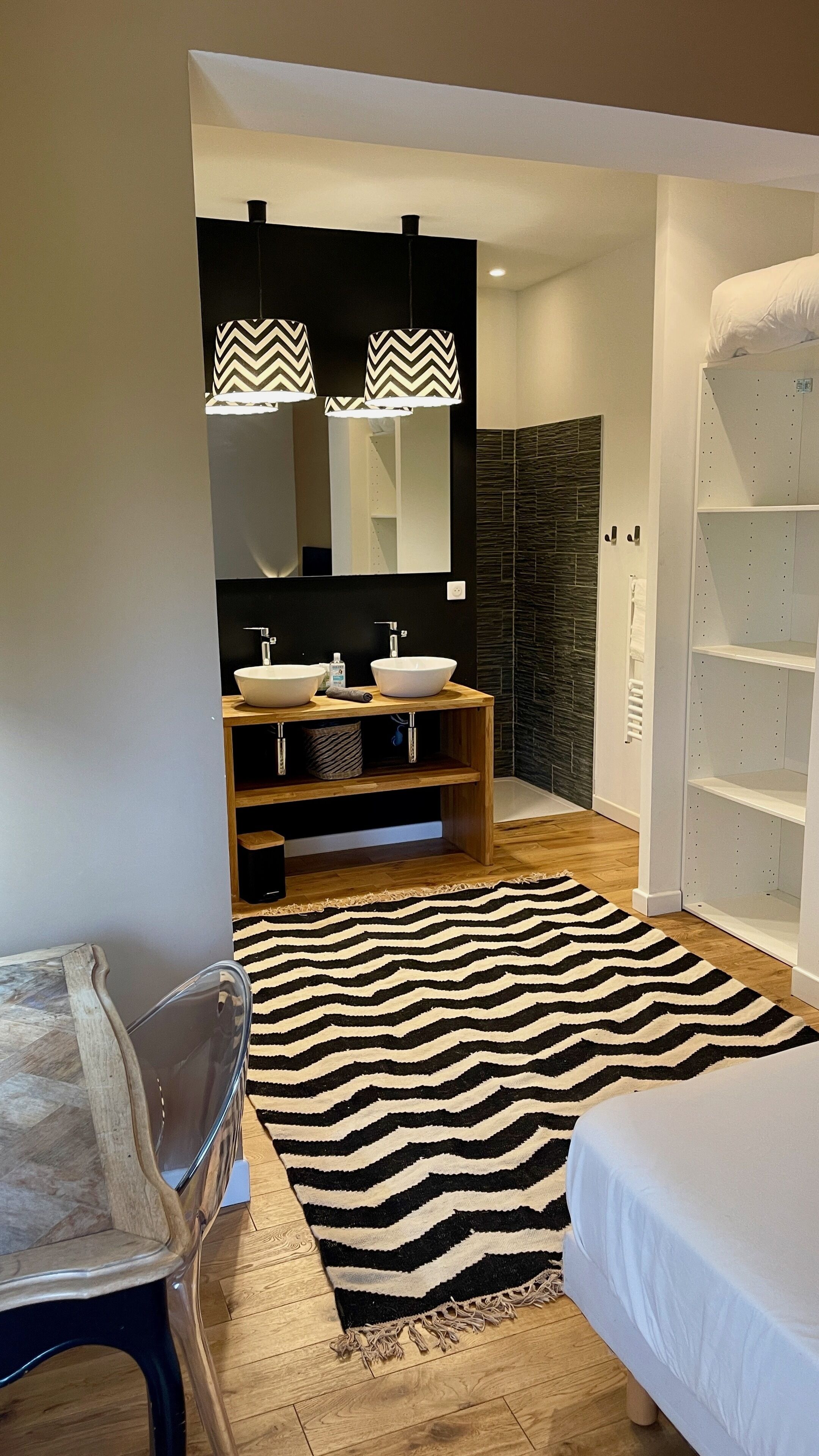 A modern bathroom with a wooden vanity, two sinks, a mirror, and a black and white striped rug.