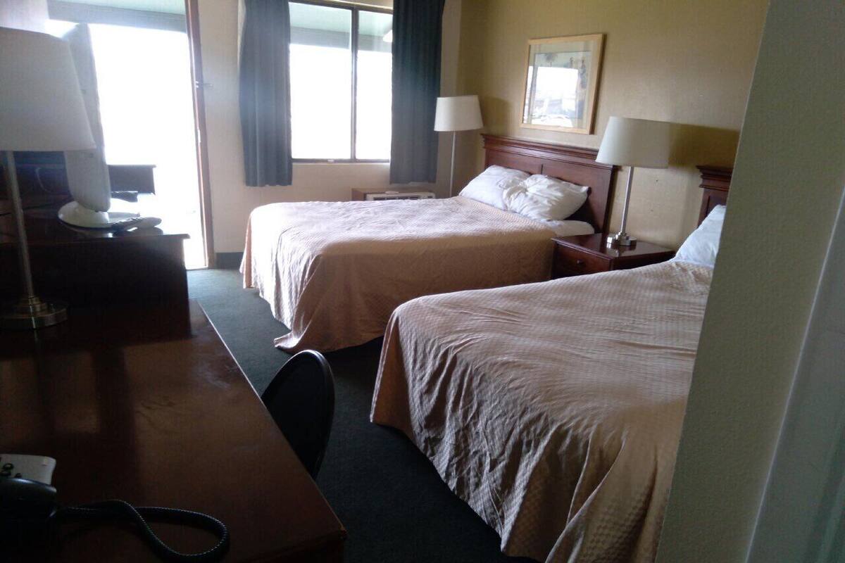 A hotel room with two beds, a desk with a telephone, and lamps.