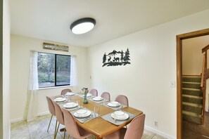A dining room with a wooden table set for six, pink chairs, a window with a view of trees, and a wall decal of a forest scene. - Timber Height's, Classy home in the pines. (Dunsmuir)