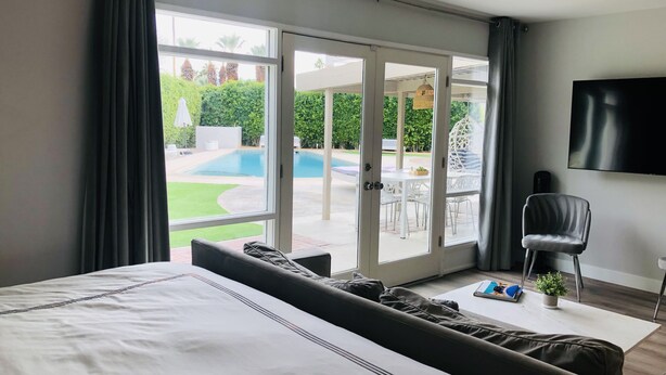 Un dormitorio con una cama grande, televisión y vistas a una piscina a través de una puerta corrediza de vidrio.
