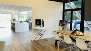 Una cocina moderna con una isla central, un comedor con mesa de madera y sillas blancas, y un amplio ventanal con vistas al exterior.