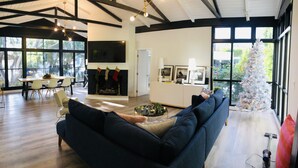 Una sala moderna con un sofá azul oscuro, un comedor con una mesa y sillas de madera, y un árbol de Navidad blanco.