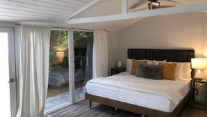 Un dormitorio con cama, mesita de noche, ventilador de techo y puerta corrediza de vidrio que da a un espacio exterior.
