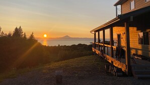 A wooden cabin with a deck overlooking a body of water and a mountain in the distance.