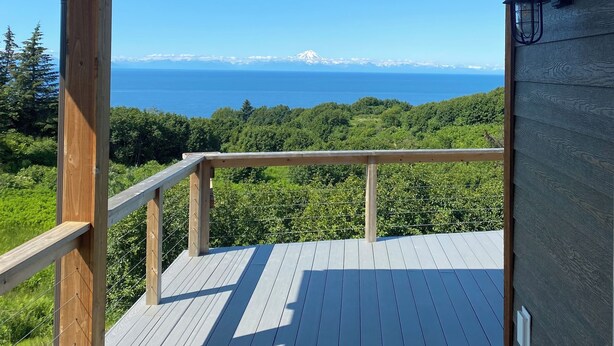 A wooden deck with a railing overlooking a mountainous landscape and a body of water.