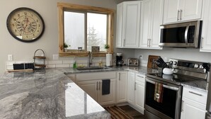 A modern kitchen with white cabinets, stainless steel appliances, a marble countertop, and a large wall clock.
