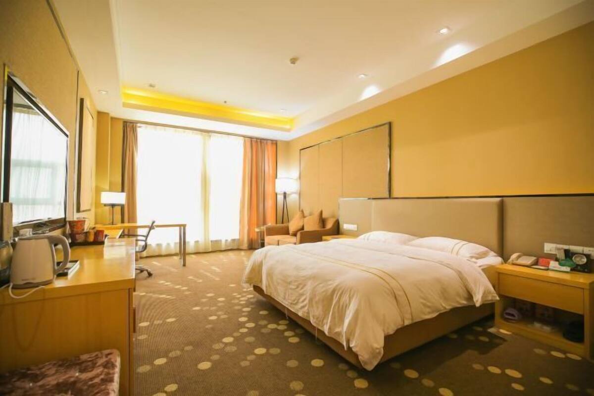 Une chambre d’hôtel avec un grand lit, un bureau avec une chaise, une petite table et une table de chevet avec un téléphone.