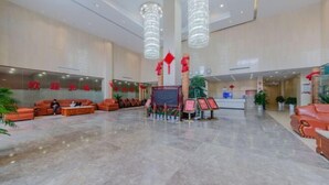 A spacious lobby with a marble floor, red couches, and a reception desk. - Meicheng Huatian Holiday Hotel (Anhua)