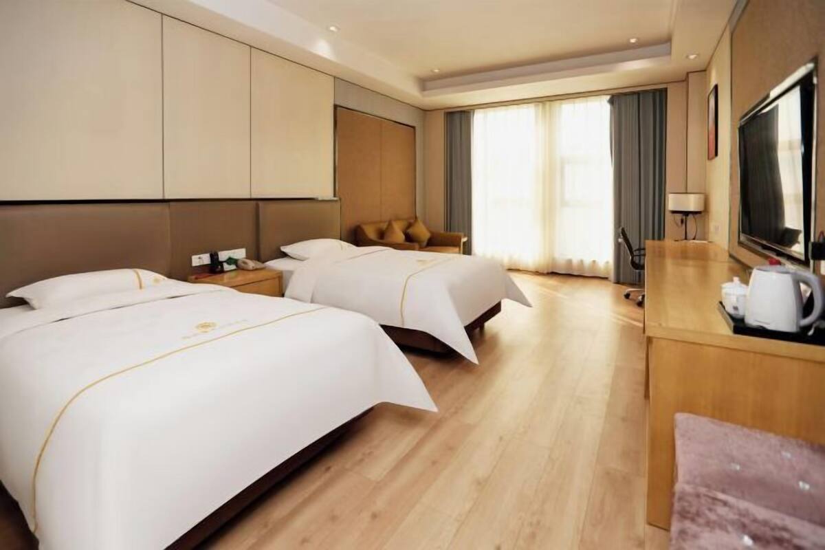 Une chambre d’hôtel avec deux lits, un bureau avec une télévision et une grande fenêtre avec des rideaux.