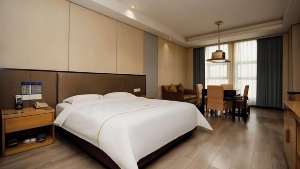 A hotel room with a large bed, a desk, and a dining area. - Meicheng Huatian Holiday Hotel (Anhua)
