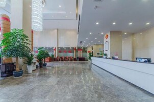 A spacious lobby with a reception desk, potted plants, and a modern chandelier.