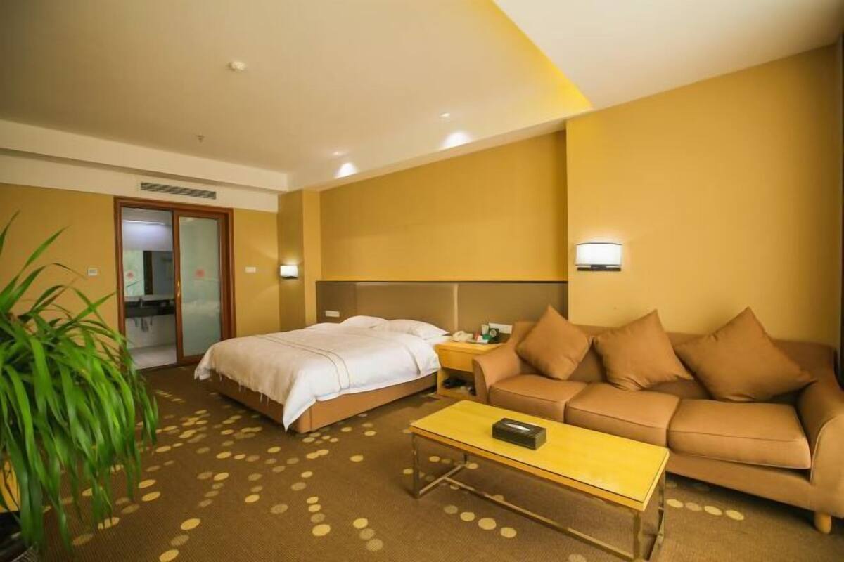 Une chambre d’hôtel avec un lit, un canapé, une table basse et une plante.