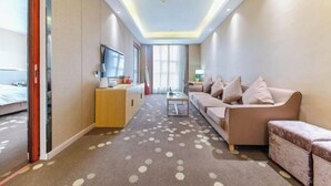 A modern hotel room with a sofa, a small table, a TV, and a bed. - Meicheng Huatian Holiday Hotel (Anhua)
