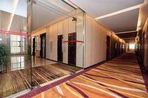 A hotel corridor with glass doors, a patterned carpet, and a long hallway.