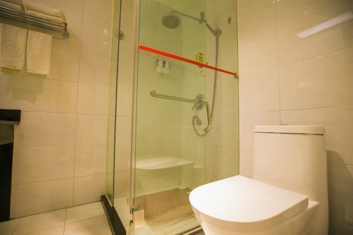 Une salle de bain avec une douche à parois de verre, des toilettes blanches et un porte-serviettes avec des serviettes.