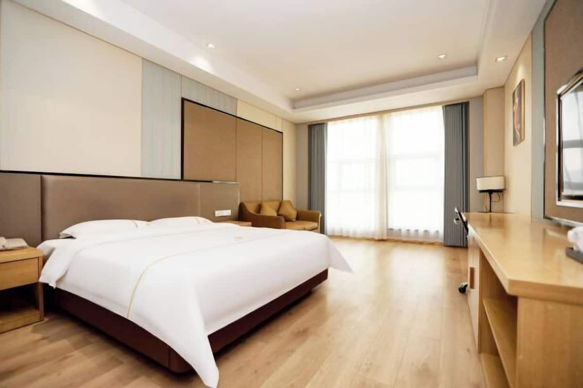 Une chambre d’hôtel moderne avec un grand lit, un bureau en bois, un canapé et une grande fenêtre avec des rideaux.