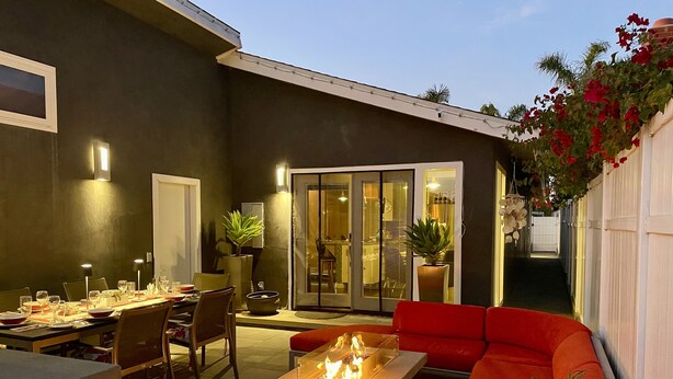 An outdoor patio with a dining table set for two, a fire pit, and a red sofa. - Modern Beach Bungalow, walk to beach, family and dog friendly (Oxnard)
