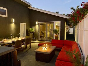 Une terrasse extérieure avec une table à manger pour deux personnes, un foyer et un canapé rouge.