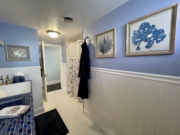 Une salle de bain avec un sol carrelé, un lavabo, un miroir et des œuvres d’art encadrées accrochées au mur.