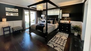A four-poster bed with a canopy, a bedside table, a lamp, a mirror, and a potted plant. - Modern Beach Bungalow, walk to beach, family and dog friendly (Oxnard)